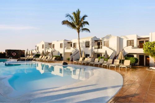 a large swimming pool with chairs and a palm tree at R2 Bahia Kontiki in Puerto del Carmen