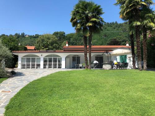 a house with palm trees in front of a yard at Casa Blanca - Villa with pool and private beach in Lesa