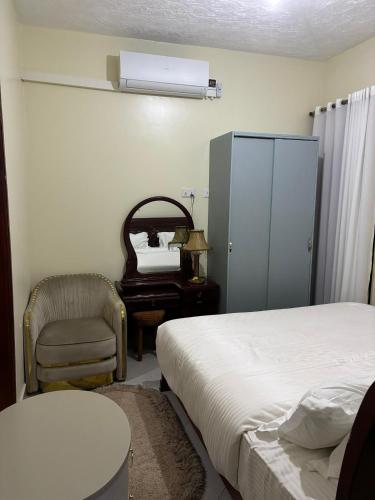 a bedroom with a bed and a chair and a mirror at Sahel Gardens in Kisubi