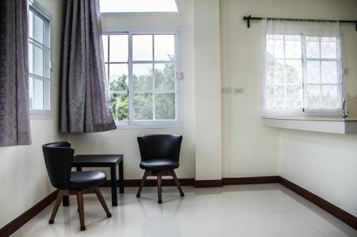 two chairs and a table in a room with two windows at Plern Pitch Residence in Pak Chong