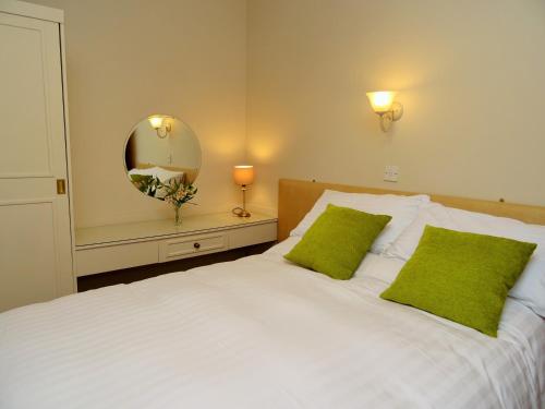 a bedroom with a white bed with green pillows and a mirror at Grisdale View in Penrith