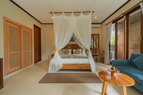 a bedroom with a canopy bed and a blue couch at Budhi Ayu Villas and Cottages Ubud by Mahaputra in Ubud