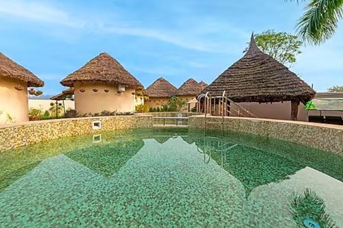 a swimming pool in front of two huts and a building at Forest Mud Villas in Haridwār
