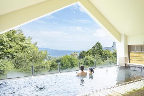 two people in a swimming pool with a large window at Ooedo Onsen Monogatari Hotel Ranpu in Hirado