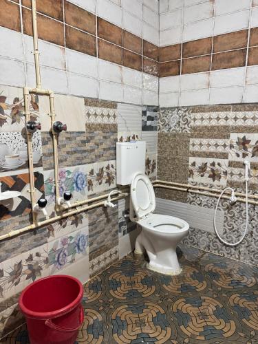 a bathroom with a toilet and a red bucket at Junglee tree stays in Hampi