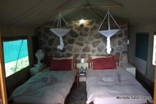 a bedroom with two beds and a stone wall at Mondjila Safari Camp in Okaukuejo