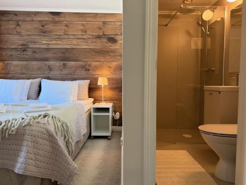 a bedroom with a wooden wall and a bed and a bathroom at Strandlogiet Ljugarn in Ljugarn