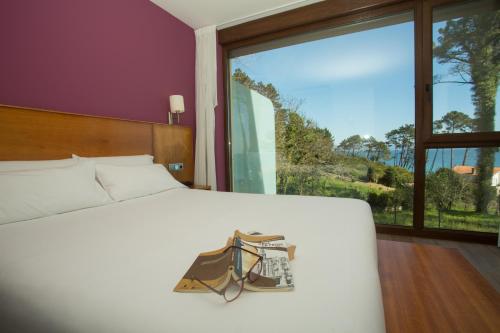 a bedroom with a white bed and a large window at Hotel Alén do Mar in Finisterre