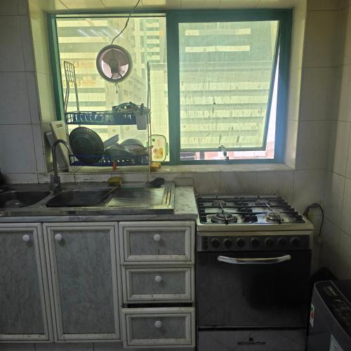 a kitchen with a stove and a sink and a window at Bedroom with shared kitchen men only in Sharjah