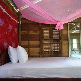 a bedroom with a large bed with a pink canopy at Authentic Cambodian Angkor Cottage in Siem Reap