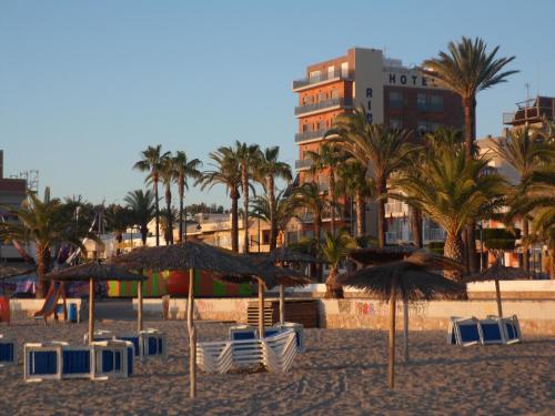 een strand met stoelen, parasols en palmbomen bij Hotel Ribera in Santiago de la Ribera