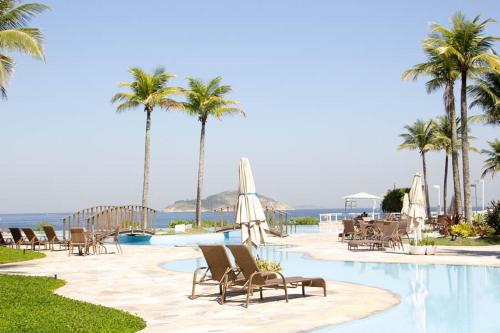 a resort with a pool with chairs and palm trees at Camboinhas Oceanside Oceanfront in Rio de Janeiro