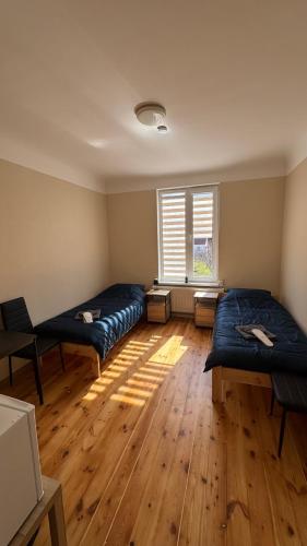 two beds in a room with wooden floors and a window at Smilšu ielas Hostelis in Valmiera