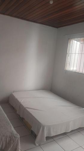 a bed in a white room with a window at Quarto do aconchego in Caraguatatuba