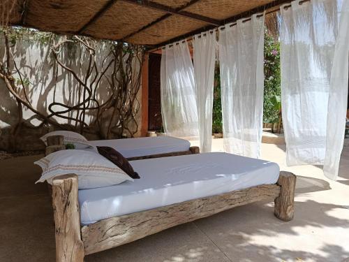 two beds in a room with white curtains at Maison Talouma in Saly Portudal