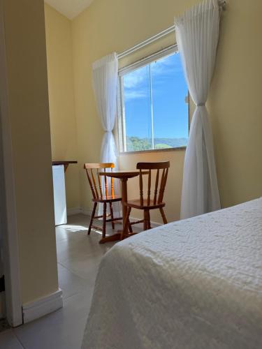 a bedroom with a bed and two chairs and a window at Suíte confortável no centro da cidade in Miguel Pereira