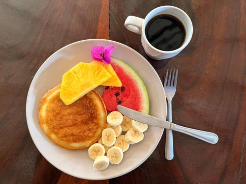 a plate of pancakes and fruit with a cup of coffee at La Posada - Hostel in Santa Teresa Beach