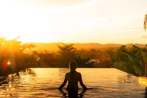 a woman sitting in the water in a pool at sunset at Villa Das Contas Boutique in Itacaré