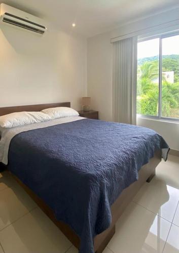 a bedroom with a bed with a blue comforter and a window at Private Pool, Walk to Beach -Los Delfines in Paquera
