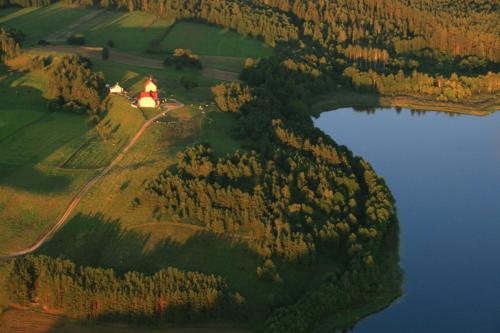 an island with a house on it next to a lake at Dworek Zielone Wzgórza Nad Jeziorem in Postawele