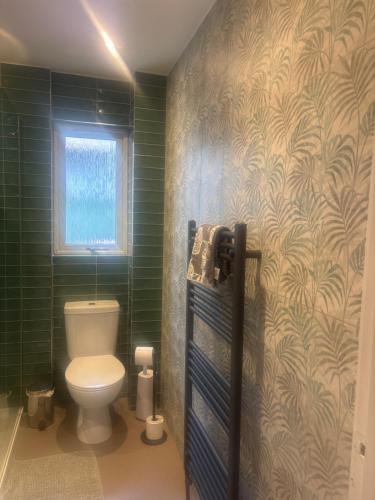 a bathroom with a toilet and green tiled walls at Linmore in Aviemore