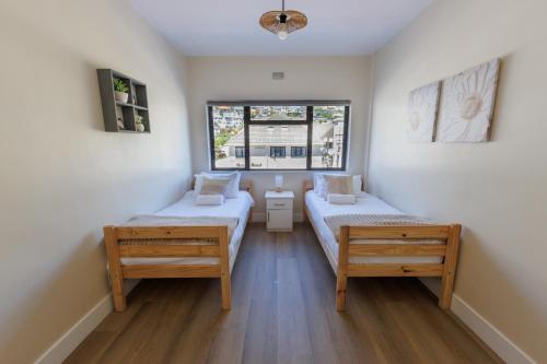 a small room with two beds and two windows at Modern Seaside Apartment in Fish Hoek