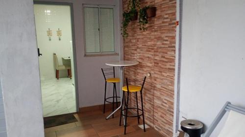 a small table and two stools in front of a brick wall at Praia Studios in Vila Velha
