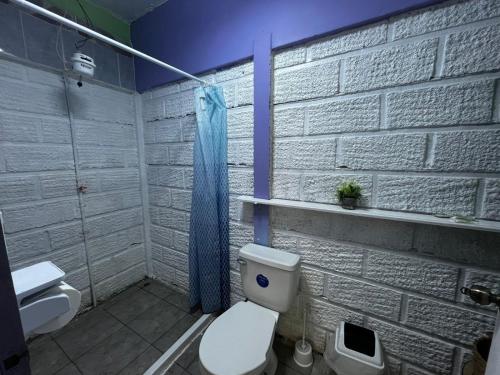 a bathroom with a toilet and a white brick wall at Habitaciones Kolibri in Quepos