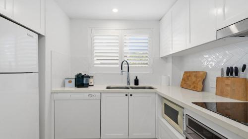 a white kitchen with white cabinets and a sink at Sea Glass in Terrigal