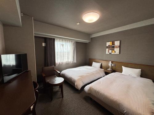 a hotel room with two beds and a flat screen tv at Hotel Route-Inn Shibukawa in Shibukawa