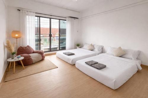 a white living room with two beds and a chair at The Layover Donmueang Airport Hostel in Thung Si Kan