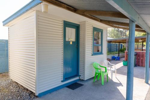 a tiny house with a blue door and two green chairs at North South Holiday Park in Christchurch