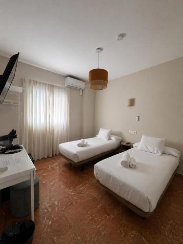 a room with two beds and a desk and a television at La Vega Rooms in Huelva