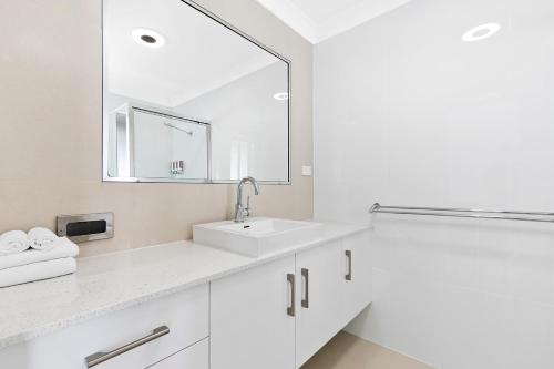 Baño blanco con lavabo y espejo en Casa Nostra Motel, en Rockhampton