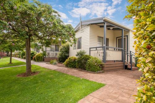 a white house with a porch and a yard at Warragul Gardens Holiday Park in Warragul