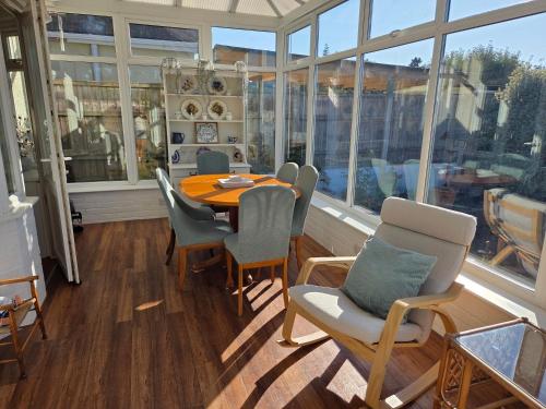 a dining room with a table and chairs and windows at Cosy Bournemouth Bungalow in Longham