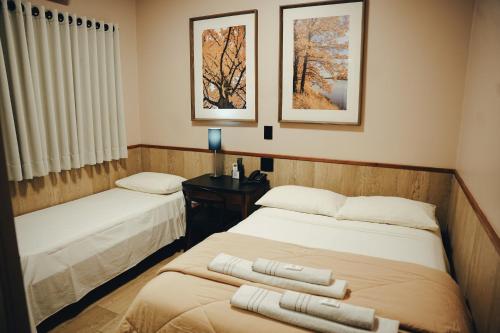 two beds in a room with two pictures on the wall at Candeias Hotel in Batatais