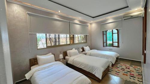 a bedroom with three beds and two windows at Villa familiale avec piscine privée sans vis à vis in Oulad Raho