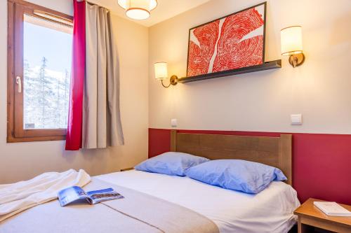 a bedroom with a bed with two blue pillows and a window at Résidence Pierre & Vacances l'Albane in Vars