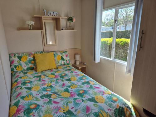 a bedroom with a bed with a floral comforter and a window at Becky's Caravan at Marton Mere in Blackpool