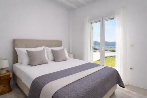 a white bedroom with a large bed and a window at White Villa Milos in Adamantas