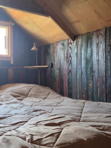 a bed in a room with a wooden wall at Ardennen Kotje in Durbuy