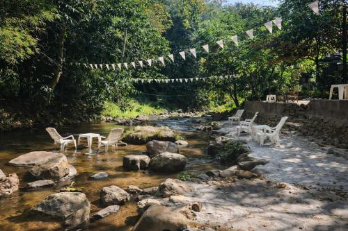 a stream with white chairs and a bridge with flags at 1000 Stars Riverside Hostel in Ban Khrae Yao Doi Bo