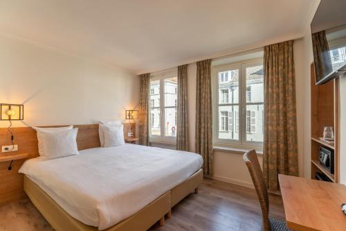a bedroom with a bed and a desk and windows at Hotel Bryghia in Bruges