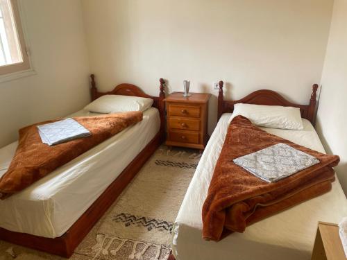 ein Schlafzimmer mit zwei Betten und einem hölzernen Nachttisch in der Unterkunft Dâr Mâbâ in Tazenakht