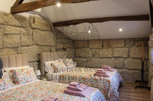a bedroom with two beds and a stone wall at Quinta das Flores da Mãe in Folhada