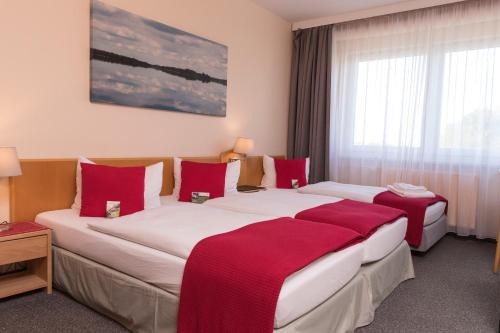 two beds in a hotel room with red pillows at Hotel am Tierpark in Güstrow