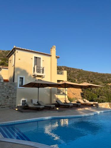 ein Swimmingpool mit Sonnenschirmen und Liegestühlen neben einem Haus in der Unterkunft August Andros in Ándros