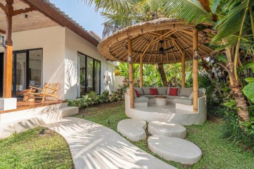 a patio with a couch under a straw umbrella at Sicilia Villa - Ubud Pool Stay with Open-Air Bath & Gazebo in Ubud