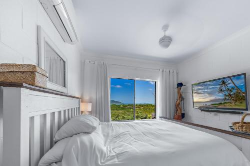 a white bedroom with a large bed and a window at Ocean's Edge in Cannonvale